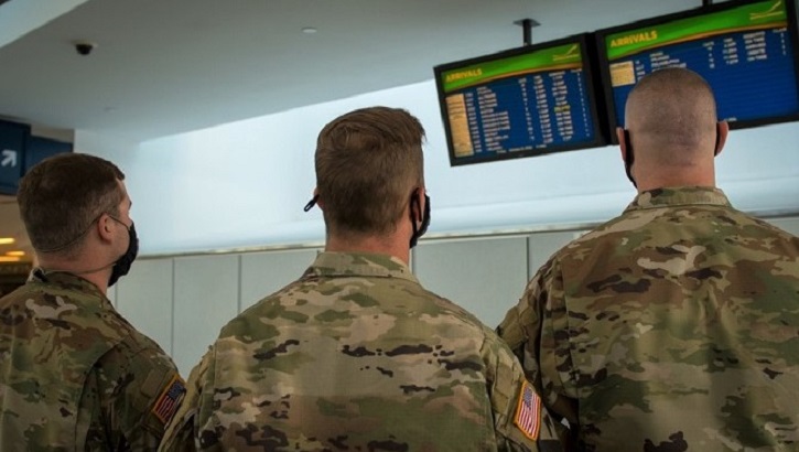 Image of Soldiers wearing masks, looking at flight information in airport.