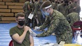 Military personnel wearing a face mask and a face shield administering the COVID-19 vaccine