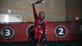 Woman in wheelchair on podium; holding up prosthetic leg