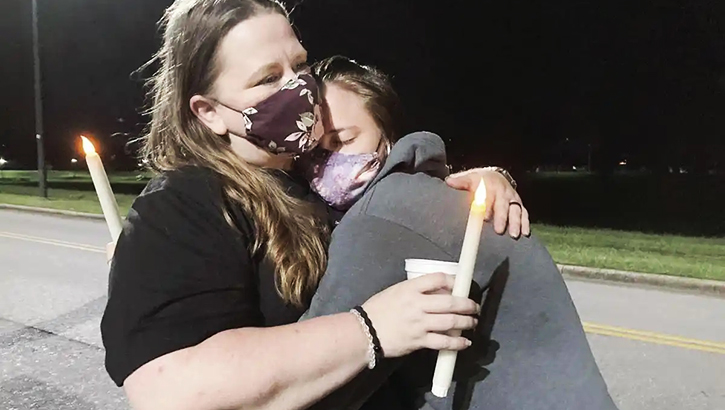 Image of Woman wearing a mask, hugging her daughter.