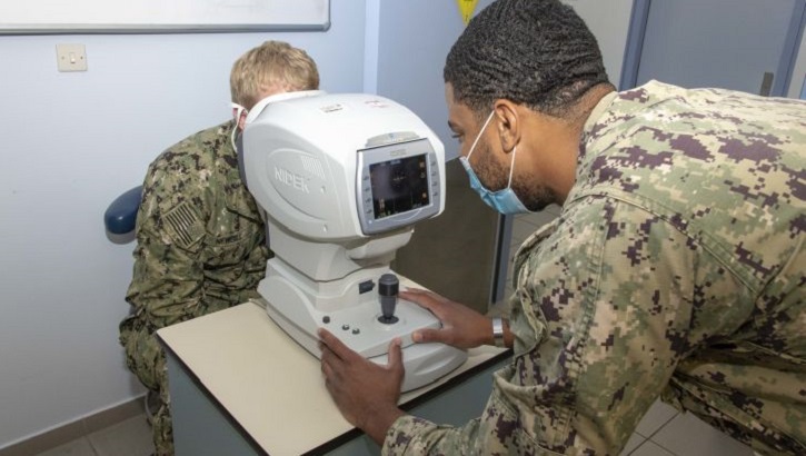 Image of military health personnel wearing a mask and performing an eye exam.
