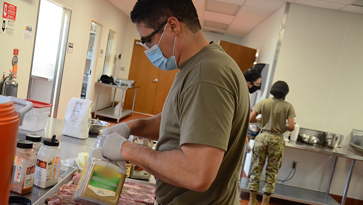 Image of Military health personnel preparing food trays while wearing a face mask.
