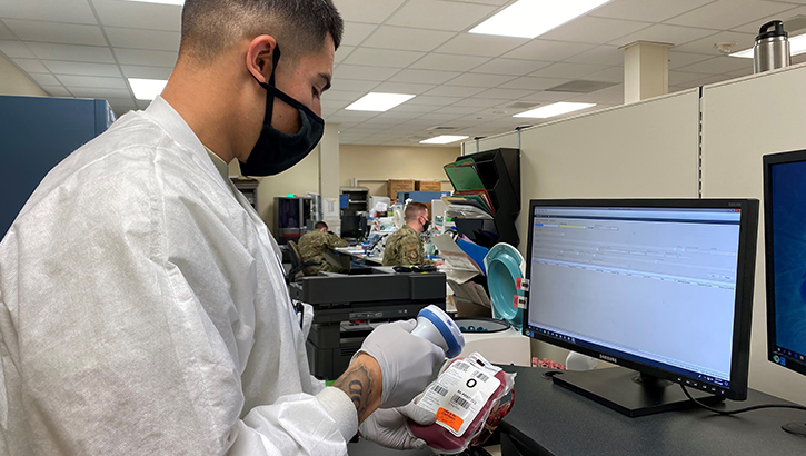Image of Technician wearing a mask, scanning in a label on a unit of blood. Click to open a larger version of the image.