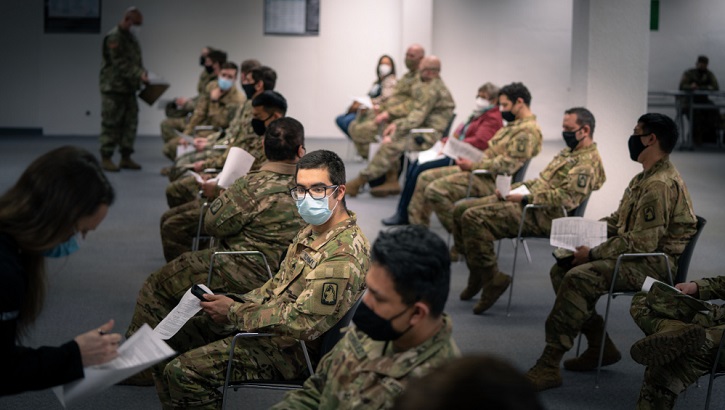 Image of Military personnel wearing face mask sitting in a line waiting for their COVID-19 vaccine. Click to open a larger version of the image.