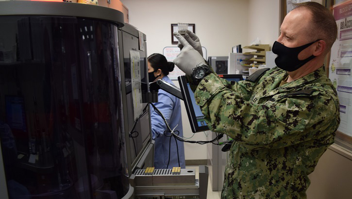 Image of Military health personnel wearing a face mask using a blood analyzer machine.