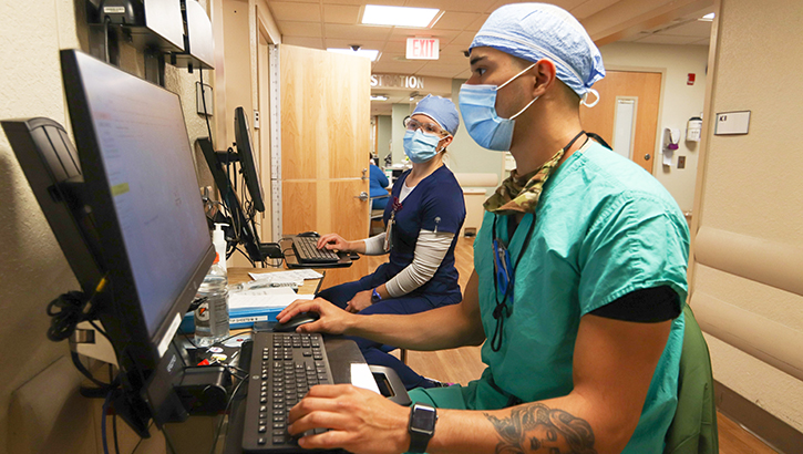 Image of Medical technicians wearing masks and entering information on a computer.