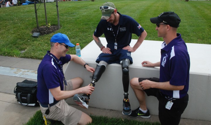 Air Force Maj. Chris Ledford (blue hat) and Army Maj. Patrick Carey (black hat) examine the prosthetic legs of British Army Trooper Chris Middleton at the Warrior Games at Marine Corps Base Quantico, Virginia. Both Ledford and Carey are sports medicine fellows at the Uniformed Services University of the Health Sciences (USU) and are part of the medical support for the competition which runs through June 28.