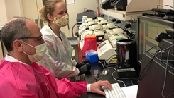 Image of two scientists in masks looking at a computer monitor