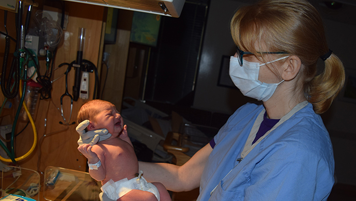 Military health personnel wearing a face mask examining a new born baby