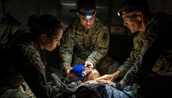 Service members practice critical airway management on a medical simulator in a low-light training scenario.