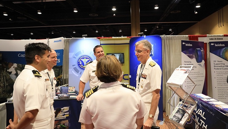 Navy Medicine West Commander Rear Adm. Tim Weber (right) discusses research findings with scientists from Navy Medicine's hospitals and research labs during the first poster session at the 2019 Military Health System Research Symposium. (U.S. Navy photo By Regena Kowitz)
