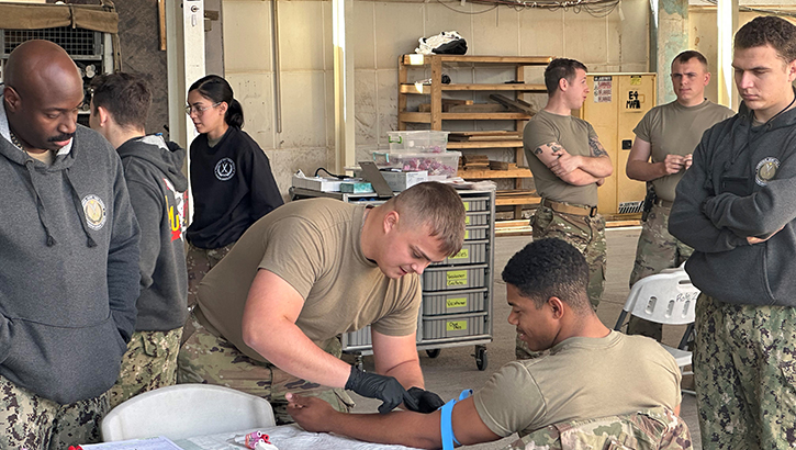 U.S. Navy Hospital Corpsman 2nd Class Freeman Morrison, a biomedical technician, left, and U.S. Navy Lt. j. g. Andrew Mappus, an emergency room nurse, right, assigned to Navy Expeditionary Medical Unit 10- Gulf, Rotation 13, are monitoring an U.S. Army Medic Task Force Buckeye, 37th Infantry Brigade Combat Team, as he draws blood from an soldier on Dec. 20. (Photo by U.S. Navy Capt. Jerrol Walla)