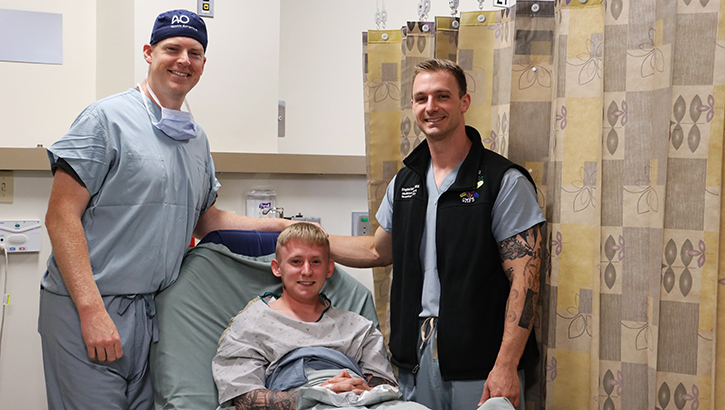 Army Spc. Grant Dickerson poses for a photo with Cmdr. Daniel Hammer, left, maxillofacial surgeon and director of the Maxillofacial Restoration Program at Naval Medical Center San Diego, and Lt. Cmdr. Stephen Moreno, oral maxillofacial surgery residency program assistant director, before he undergoes a jaw-in-a-day surgery