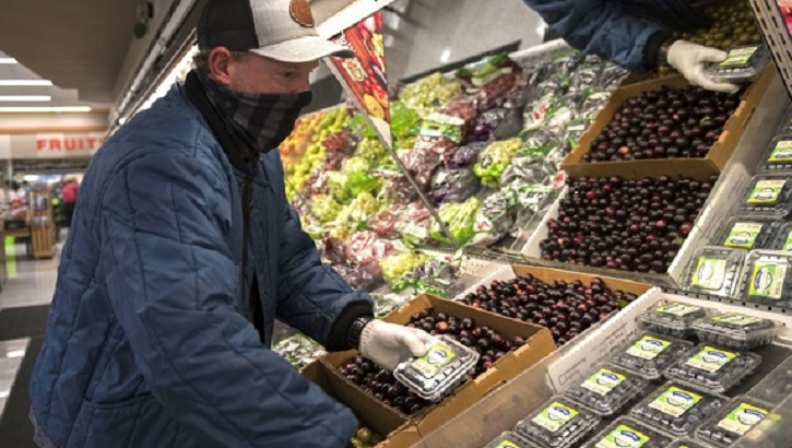 Image of Man wearing a face mask restocking fruit at a store. Click to open a larger version of the image.
