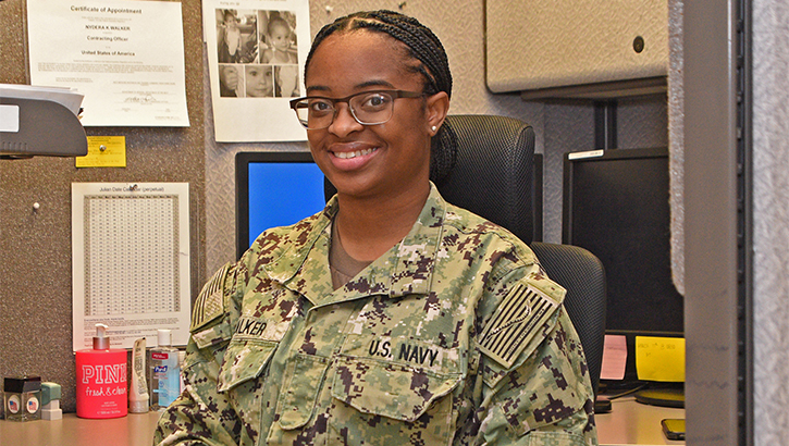 Image of Military personnel sitting in cubicle and smiling. Click to open a larger version of the image.