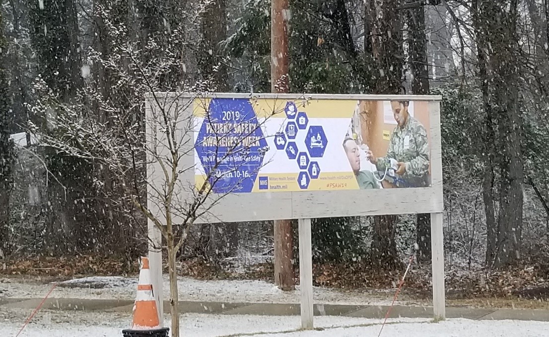 A Patient Safety Awareness Week parking lot banner hangs at the main entrance of the Defense Health Agency in Falls Church, Virginia during the week of 10-16 March 2019, showing that “We All Play a Role in Healthcare Safety”. 