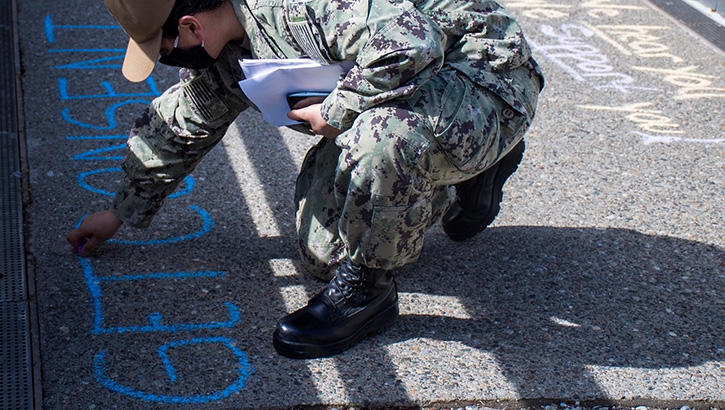 Image of Military personnel wearing a face mask writing messages with chalk on the ground.