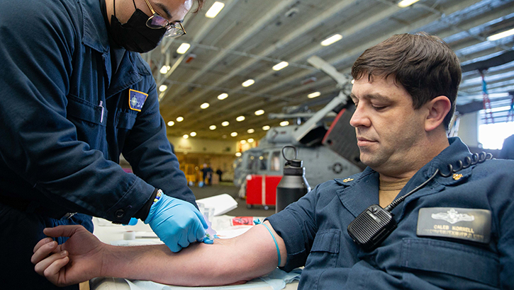 Image of U.S. Navy Chief Information Systems Technician Caleb Korrell, from Cheyenne Wells, Colorado, has his blood drawn by U,S, Navy Hospitalman Jaysean Sales, from Los Angeles, during a physical health assessment rodeo in the hangar bay on Sept. 23, 2022. The Reserve Health Readiness Program helps maintain readiness and satisfy key deployment requirements by providing medical and dental services to all National Guard, Reserve and active duty service members. (Photo by U.S. Navy Spec. 2nd Class Zack Guth).