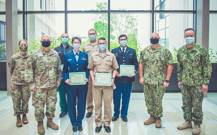 Image of Military personnel stand in front of window holding their awards. Click to open a larger version of the image.