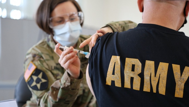 Military health personnel wearing a face mask giving someone the COVID-19 Vaccine