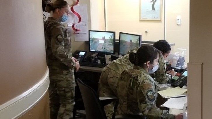 Image of Military personnel standing and sitting at a desk with multiple computer screens. Click to open a larger version of the image.