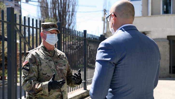 Two men (one in uniform, one not) with face masks having a discussion