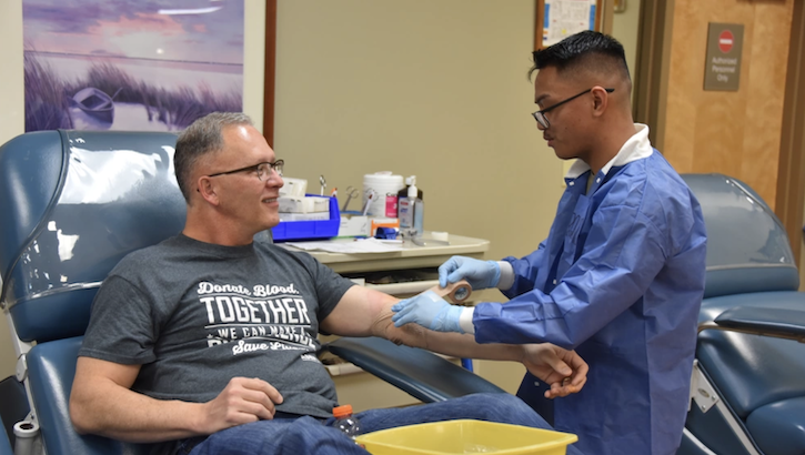 Outgoing Chief of Staff of the U.S. Army Surgeon General, U.S. Army Medical Command, and Deputy Commanding General (Support), U.S. Army Medical Command, Maj. Gen. Michael Place is assisted by Spc. Enrique Urquico, phlebotomist Fort Liberty Blood Donor Center as he completes his final blood donation as an active duty service member on Feb 16. (DHA photo by Keisha Frith)