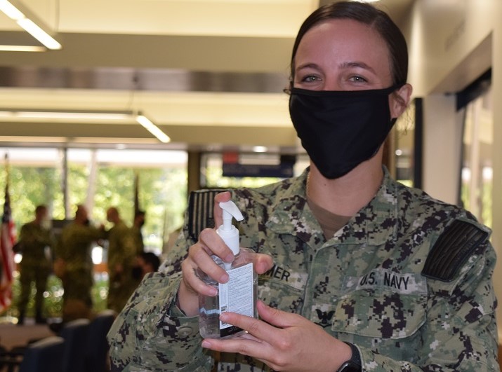 Image of Military personnel wearing a face mask while holding hand sanitizer.