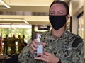 Military personnel wearing a face mask while holding hand sanitizer