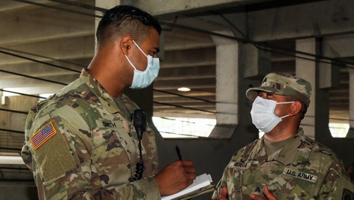 Image of Two military personnel with mask on talking, while one is writing on a notepad.