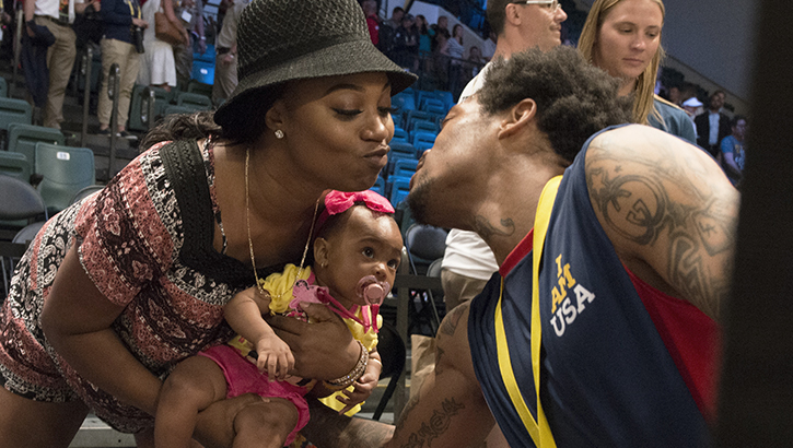 Image of Man at sporting event kissing his wife and baby.