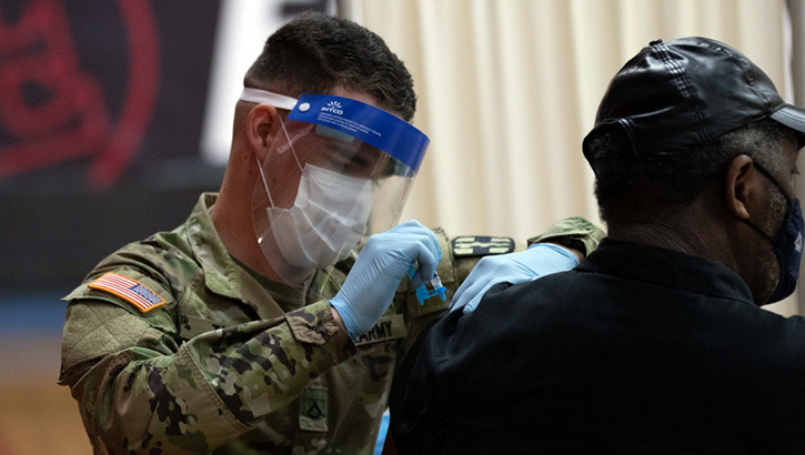 Image of Military health personnel wearing a face mask and a face shield administering the COVID-19 vaccine. Click to open a larger version of the image.
