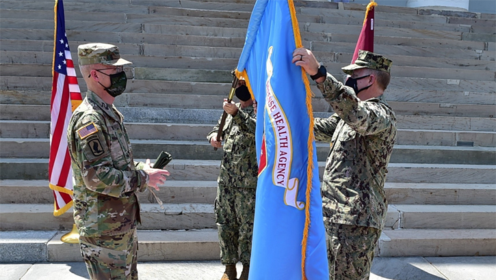 Image of Military health personnel wearing masks holding up a flag.