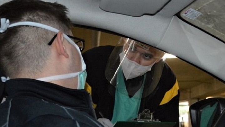 Image of Two men wearing masks, one in a car, one leaning in the car.