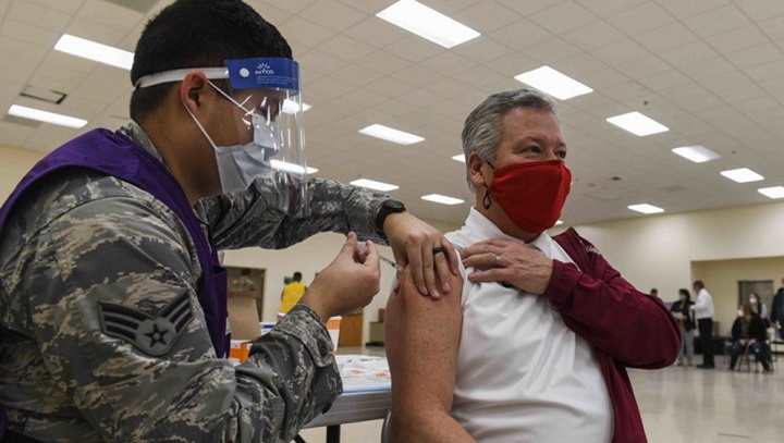 Image of Military health personnel wearing a mask giving the COVID-19 vaccine to a man who is also wearing a face mask.