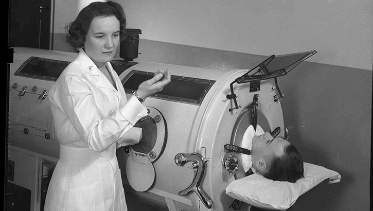 Image of Nurse checks up on a patient in a mechanical ventilator.