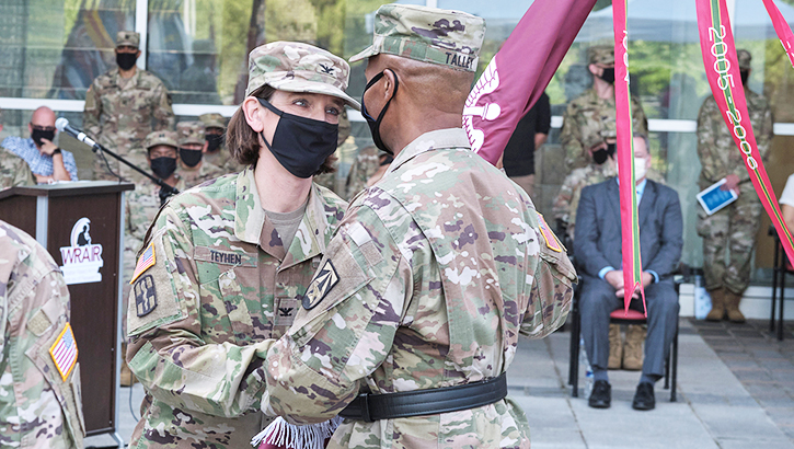 Image of Two soldiers, wearing masks, passing a flag.