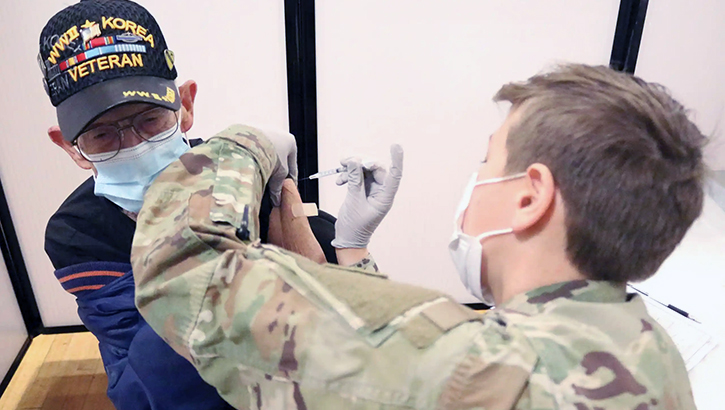 Military personnel wearing a mask, giving the COVID-19 vaccine to a veteran wearing a mask