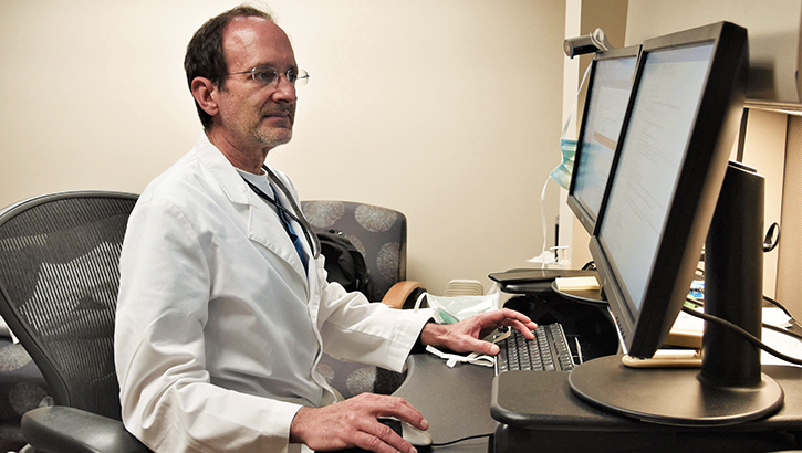 Image of Man in lab coat sitting in front of a computer screen. Click to open a larger version of the image.