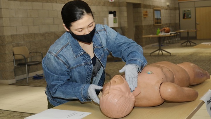 Image of Medical personnel, wearing a mask, practicing skills on a dummy.