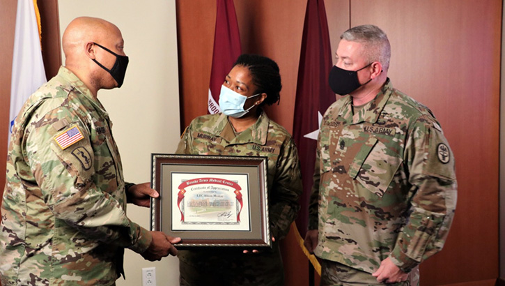 Image of Three military personnel, wearing masks, standing on a stage and holding an award. Click to open a larger version of the image.