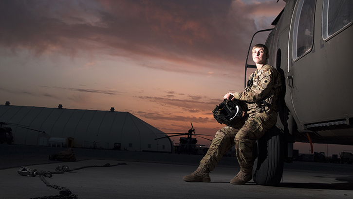 Image of Female soldier, leaning against a military vehicle, at sunset. Click to open a larger version of the image.