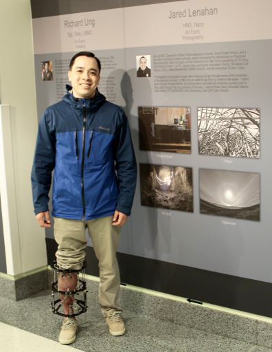 Navy Petty Officer 3rd Class Jared Lenahan poses in front of his photography display at the Wounded Warrior Healing Arts Exhibit at the Pentagon. After spending most of the past two and a half years unable to walk after a recreational rock climbing accident, Lenahan now has an external fixator on his leg which allows mobility. (Courtesy photo)