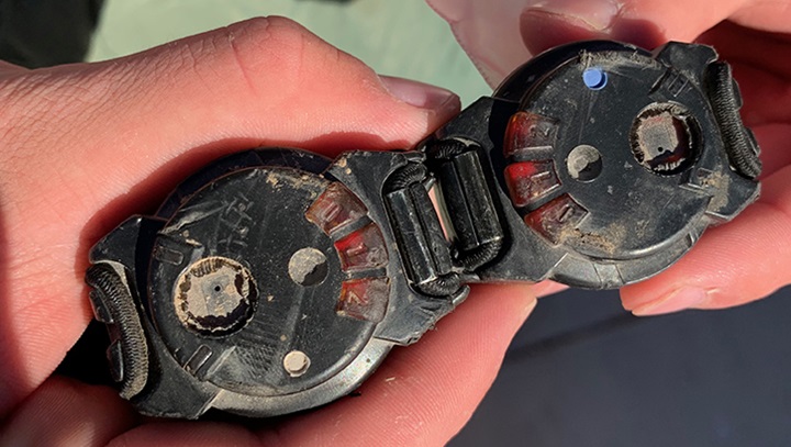 Image of Two hands holding damaged wearable blast mesurement gauges from a study on blast pressure exposure.