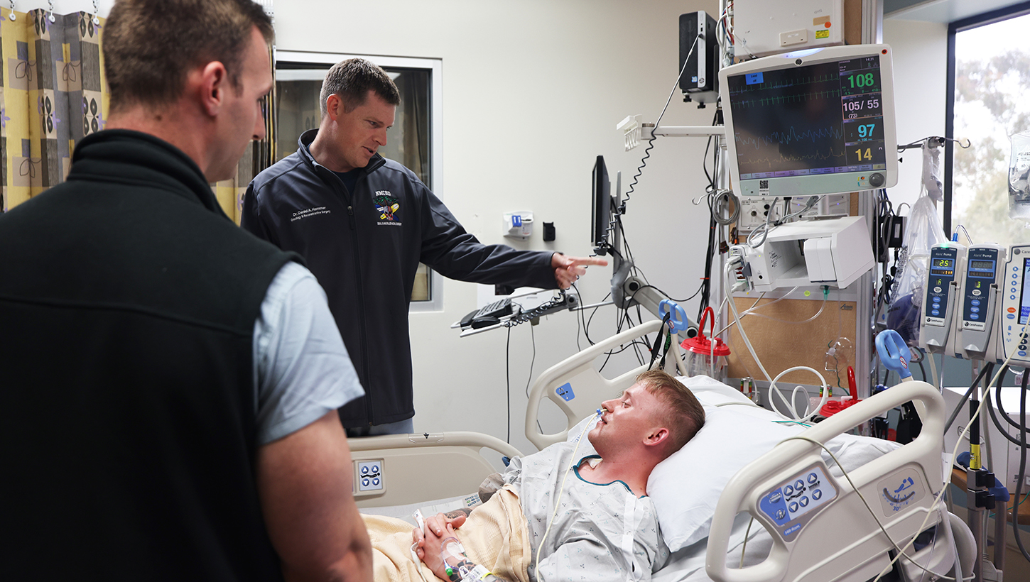 Cmdr. Daniel Hammer, left, maxillofacial surgeon and director of the Maxillofacial Restoration Program at Naval Medical Center San Diego, and Lt. Cmdr. Stephen Moreno, oral maxillofacial surgery residency program assistant director, check on U.S. Army Spc. Grant Dickerson in the intensive care unit two days after the performed his jaw-in-a-day surgery