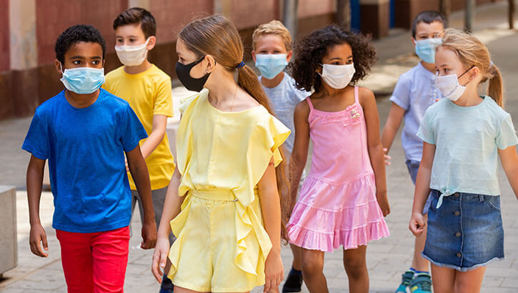 Image of A bunch of children wearing face masks walk on a city street. Click to open a larger version of the image.