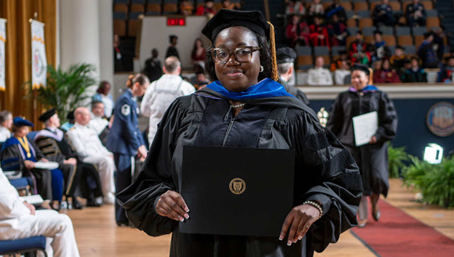 Dr. Mydirah Littlepage-Saunders holds her diploma after crossing the stage at the Uniformed Services University's 47th commencement ceremony 