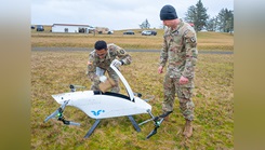 U.S. Army National Guard Sgt. 1st Class Kenneth Day retrieves simulated blood supplies delivered by a drone while U.S. Army National Guard Sgt. Keikkala provides security during a field training exercise at Camp Rilea, Oregon