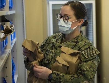Image of hospital Seaman, wearing a mask, organizing prescriptions on various shelves in a pharmacy