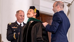 Retired Army Lt. Col. (Dr.) Ronald White (left), USU class of 2000, hoods his son, Anthony White, with the assistance of Dr. Ryan Landoll, USU, during the USU Class of  2025 Commencement ceremony